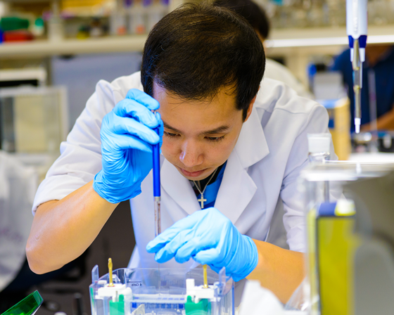 Man wearing white coat and blue gloves doing labwork in a lab setting